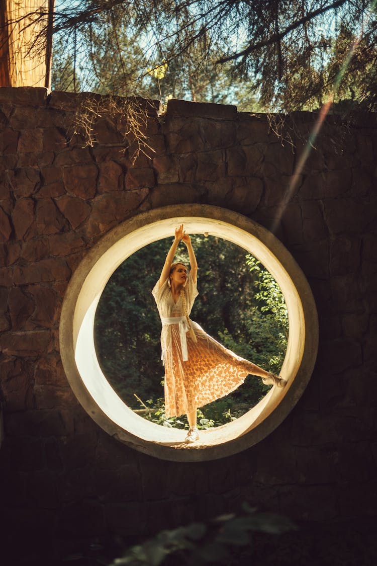 A Woman In A Dress Posing While On A Round Window