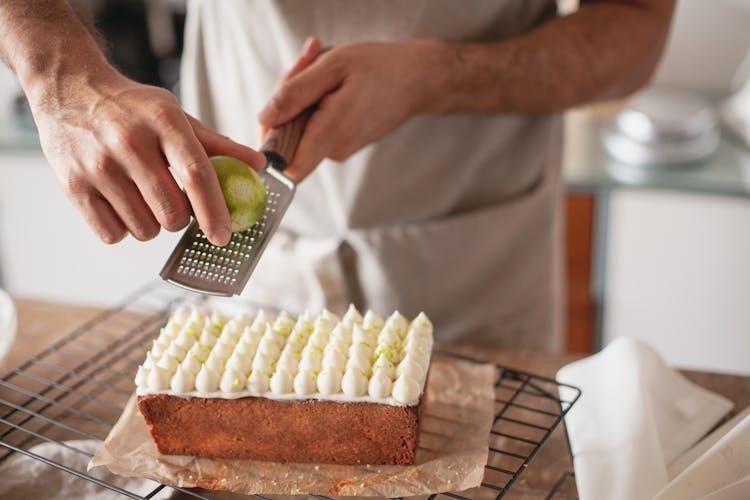 Close-up Of A Person Grating Lemon Zest Over A Cake