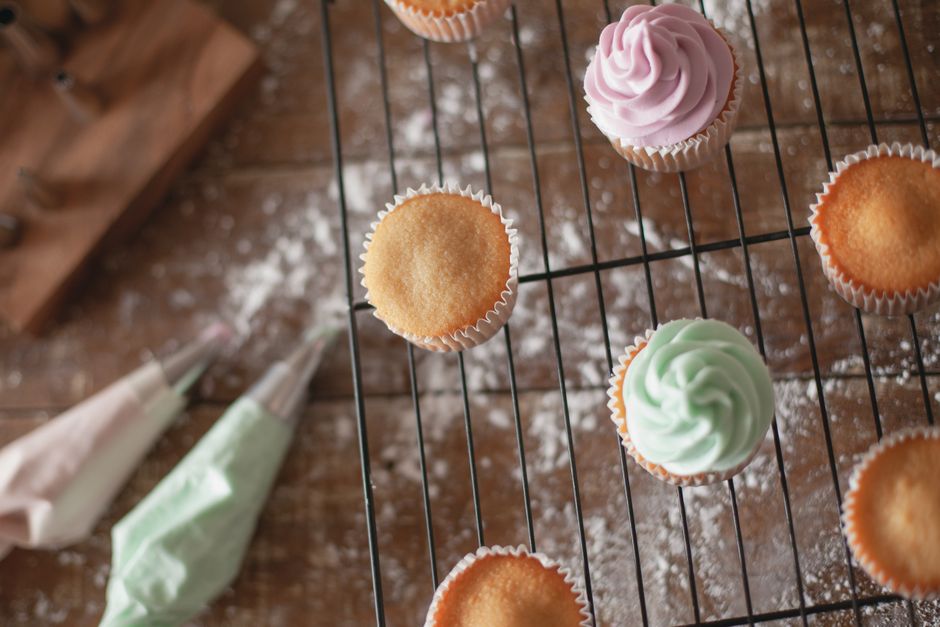 Filled piping bags beside frosted and bare cupcakes on a cooling rack. Photo by Los Muertos Crew on Pexels.