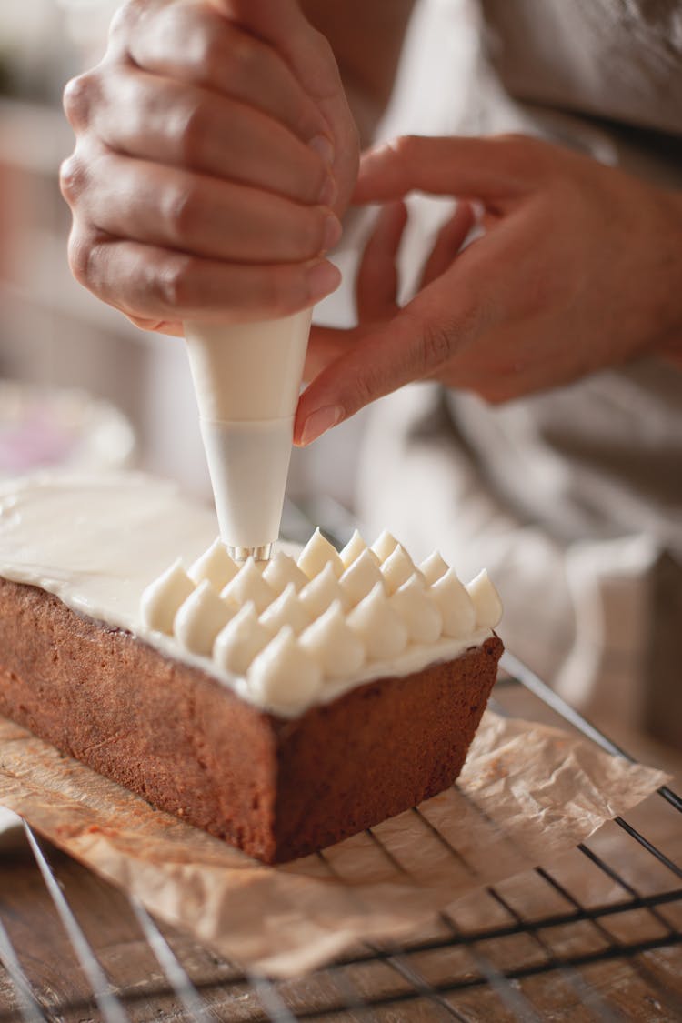 A Person Placing Icing On Top Of A Cake