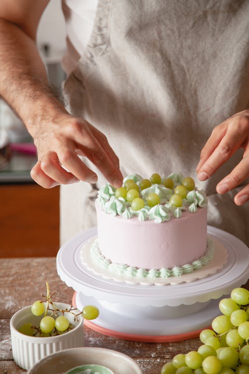 A Baker Placing Green Grapes on a Cake