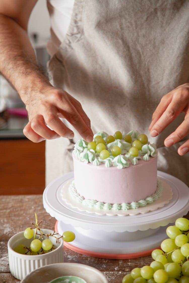 A Baker Placing Green Grapes On A Cake