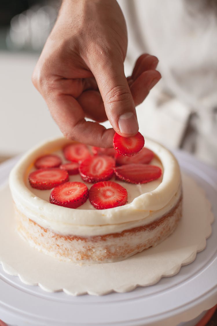 A Person Placing Strawberry Slices On Top Of A Cake