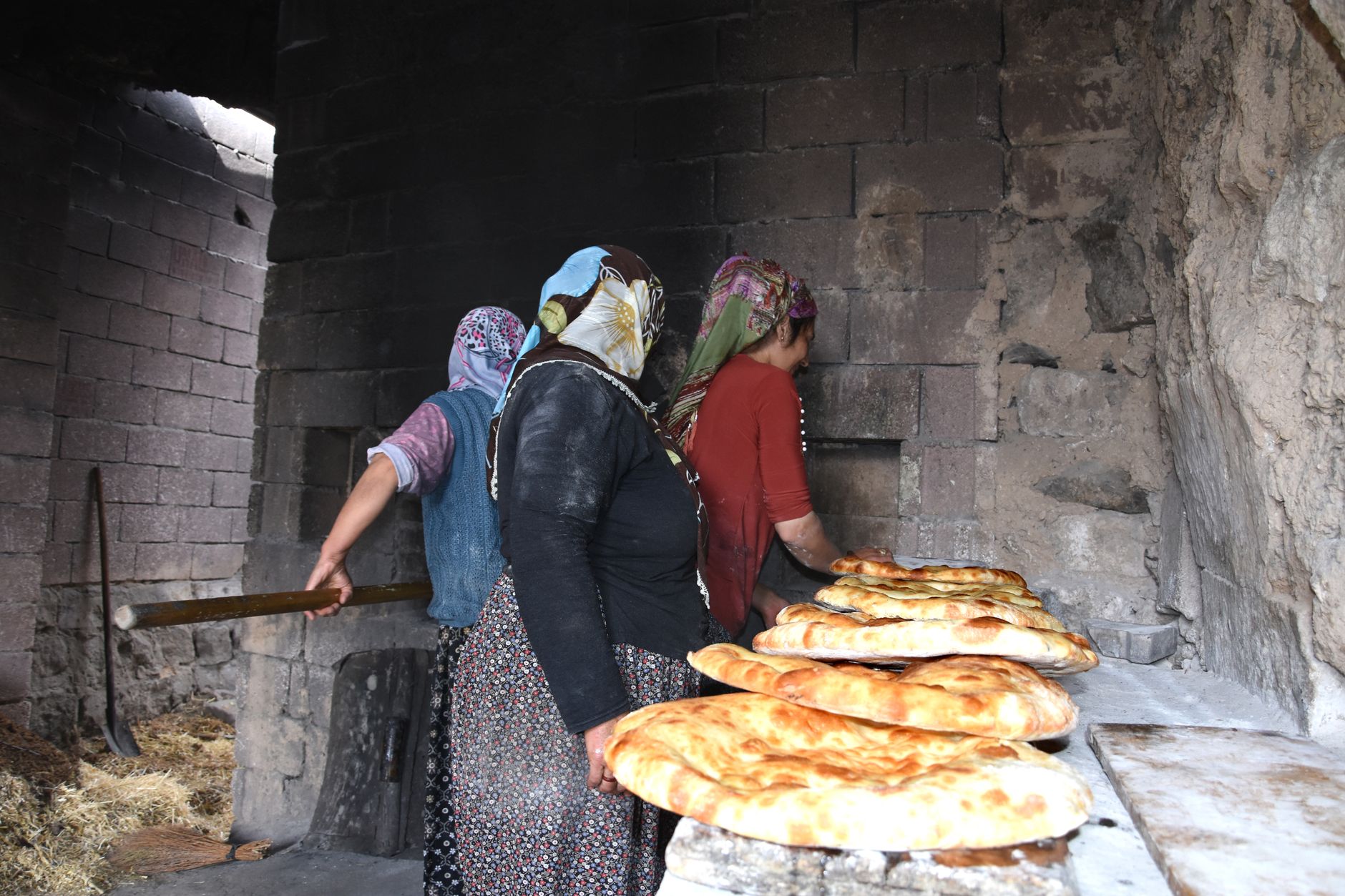 Women in traditional attire baking bread in a rustic stone oven, depicting cultural heritage.