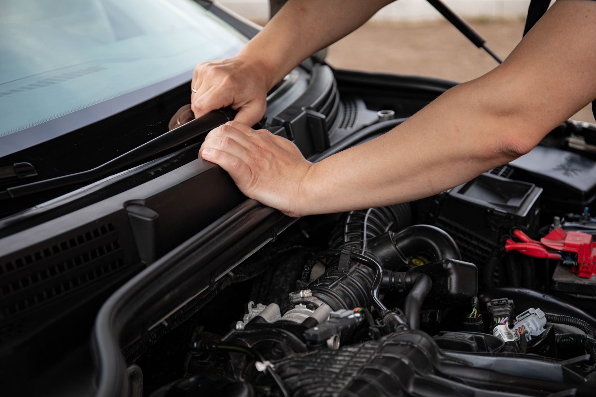 Close-up of hands repairing a car engine outdoors, focusing on automotive maintenance.