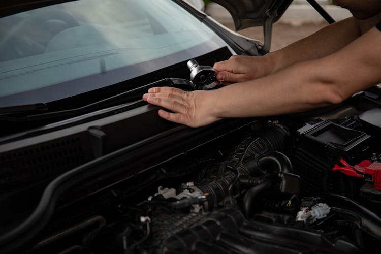 A Mechanic Holding A Ratchet Over An Engine Bay