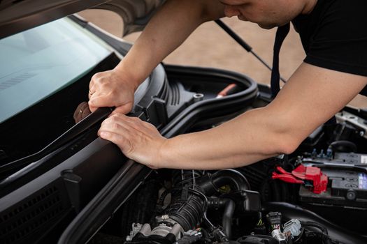 Auto mechanic working on a car engine bay, hands holding parts, outdoor setting.