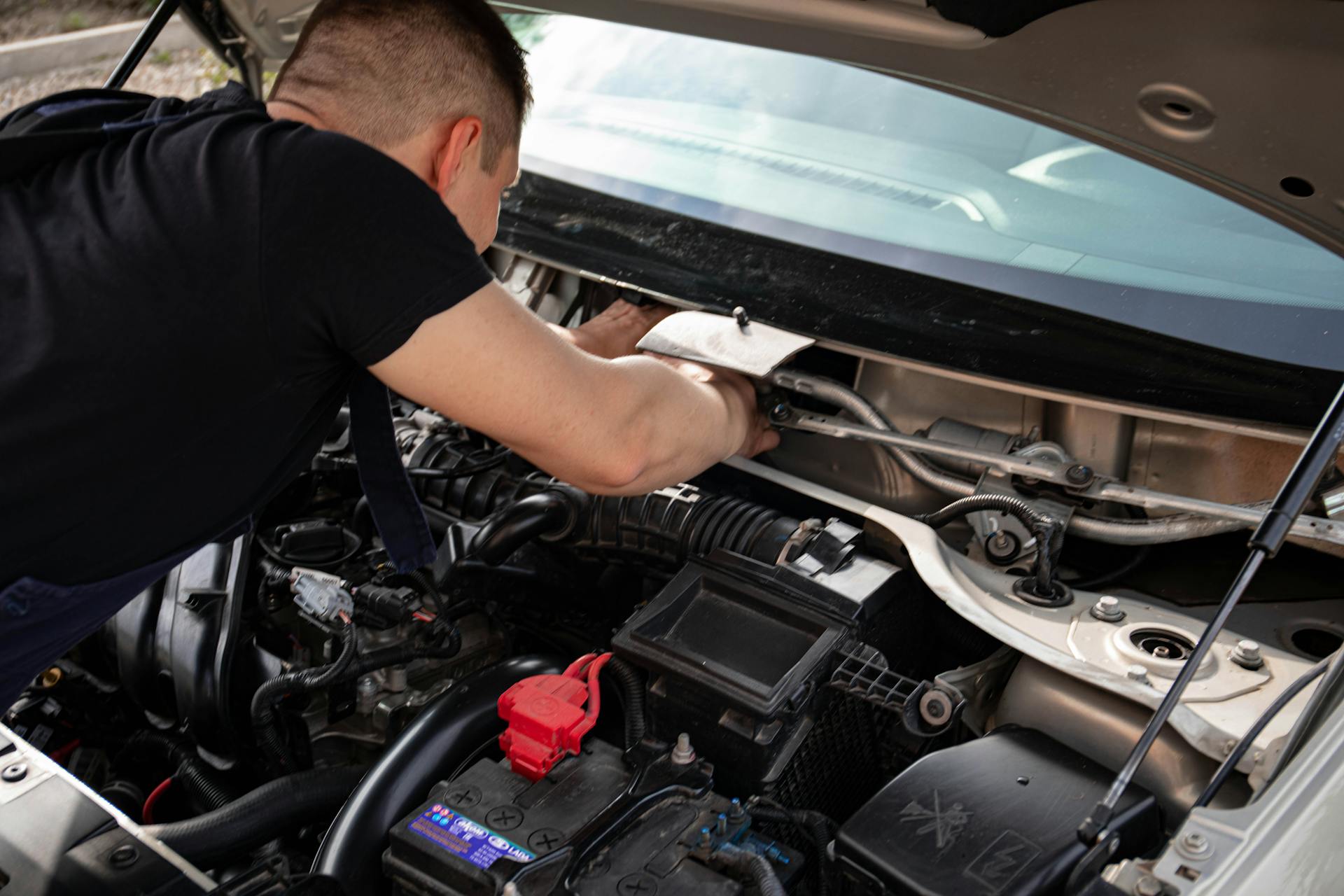 A mechanic busy repairing an engine under the hood of a car in a garage setting.