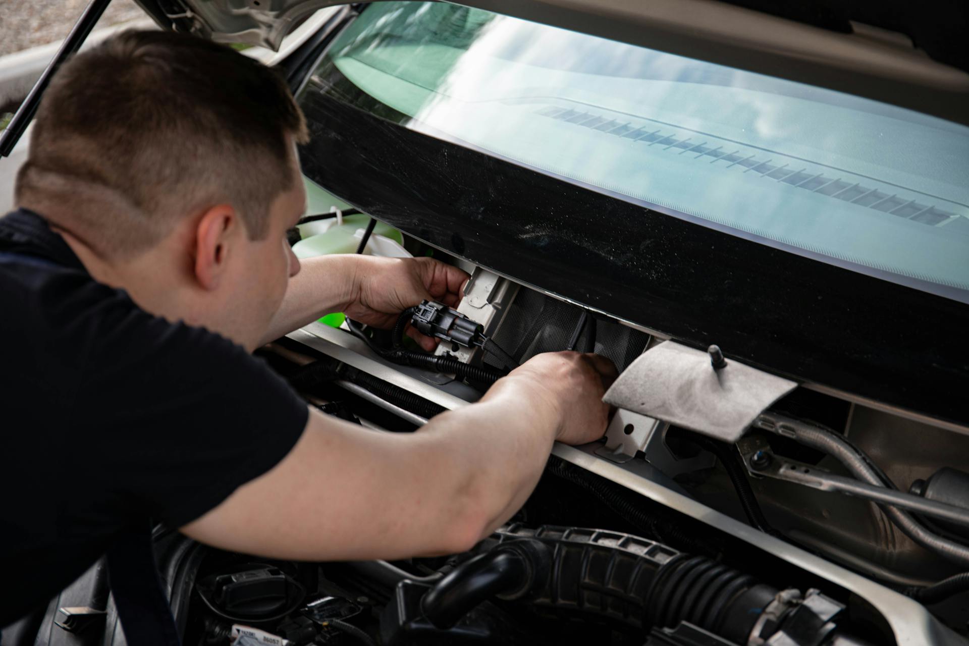 A mechanic working on car engine repairs inside a workshop setting.