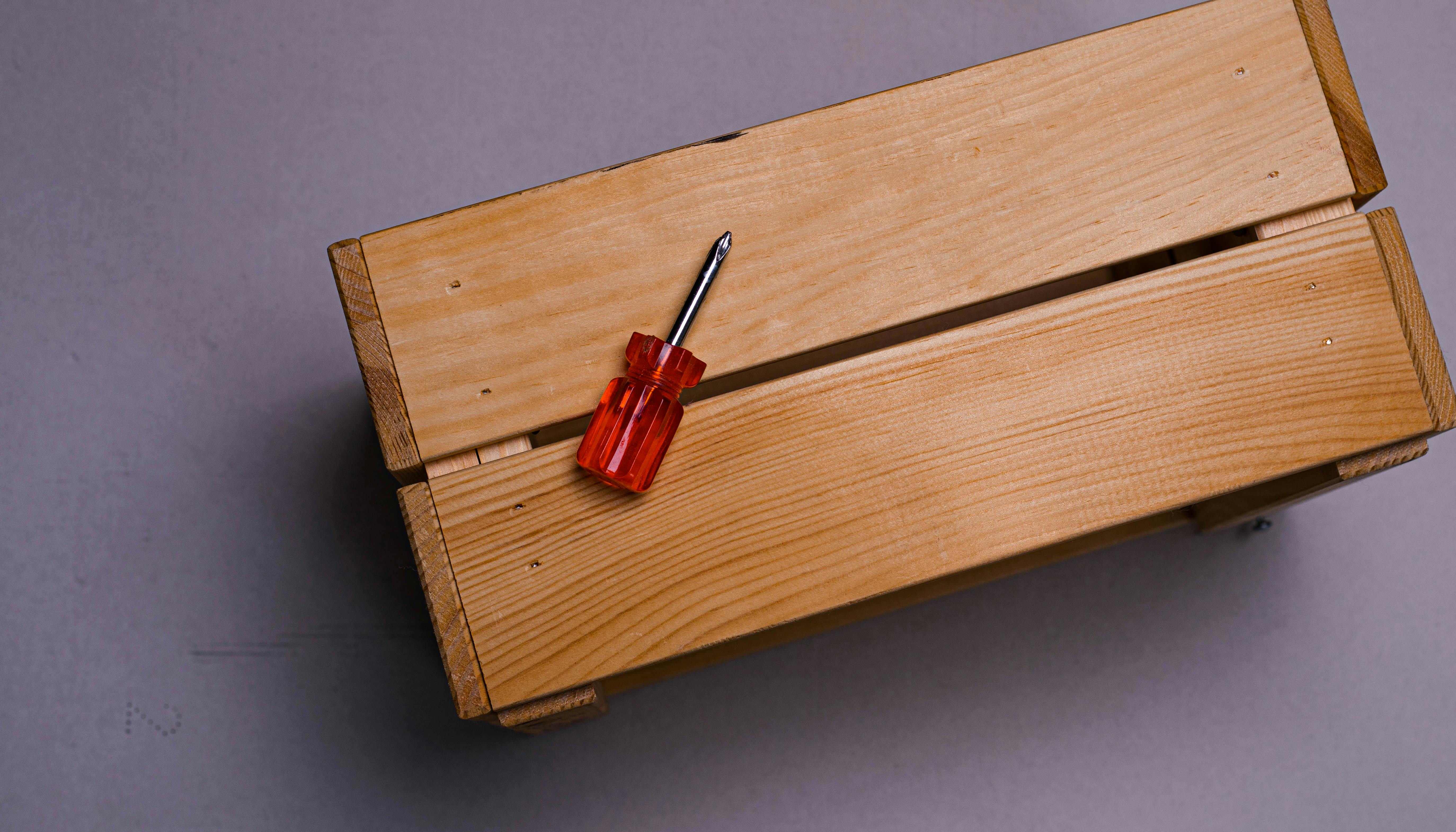 Top-down view of a wooden box with a red screwdriver on a grey background, emphasizing simplicity and utility.