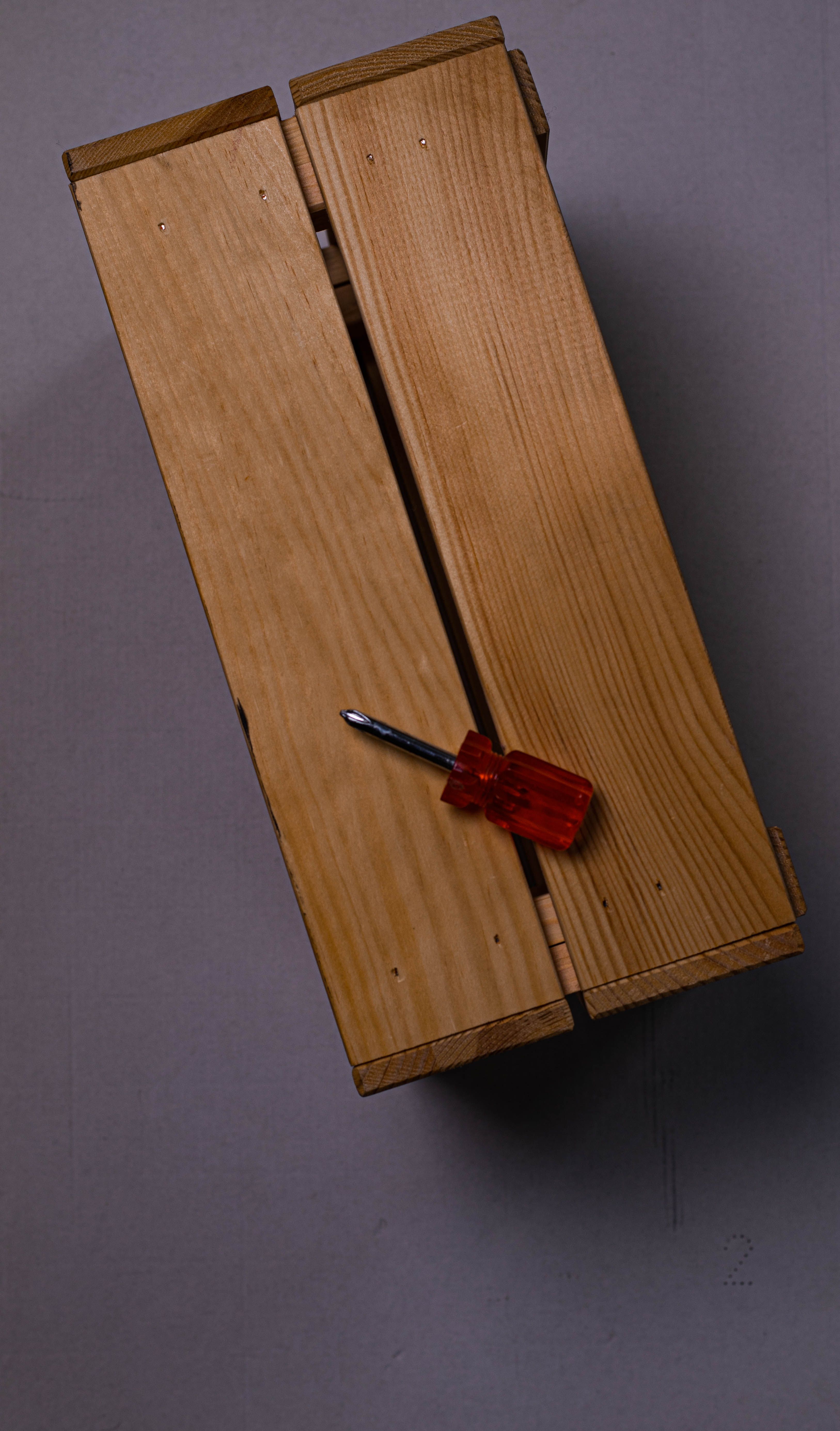 Fotomural Una toma minimalista de una caja de madera descansando sobre una superficie gris con un destornillador de mango naranja.