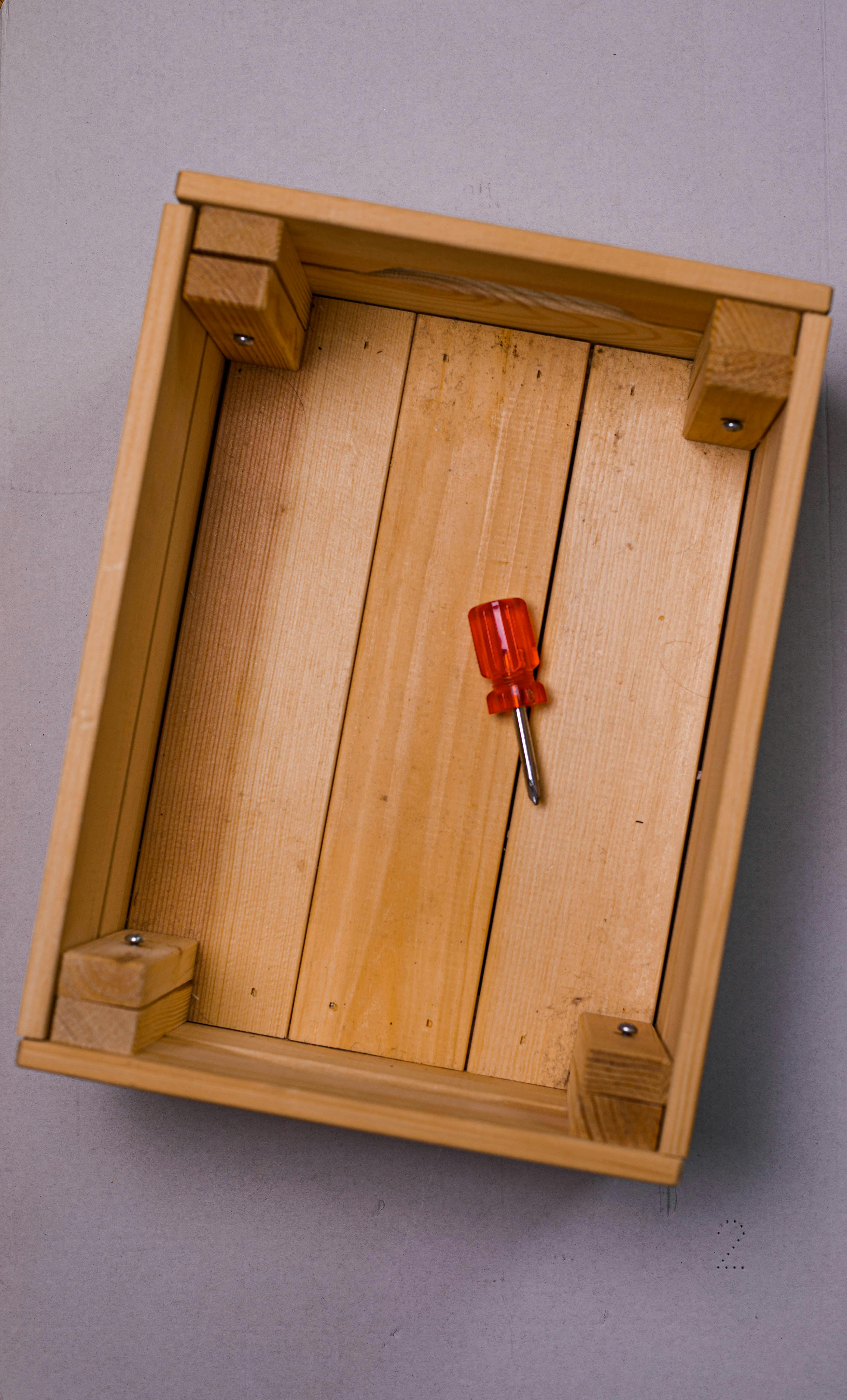 Wooden box with a red-handled screwdriver inside, seen from above. Perfect for DIY projects.