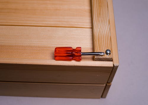 Red and Silver Screwdriver on Wood with a Nut