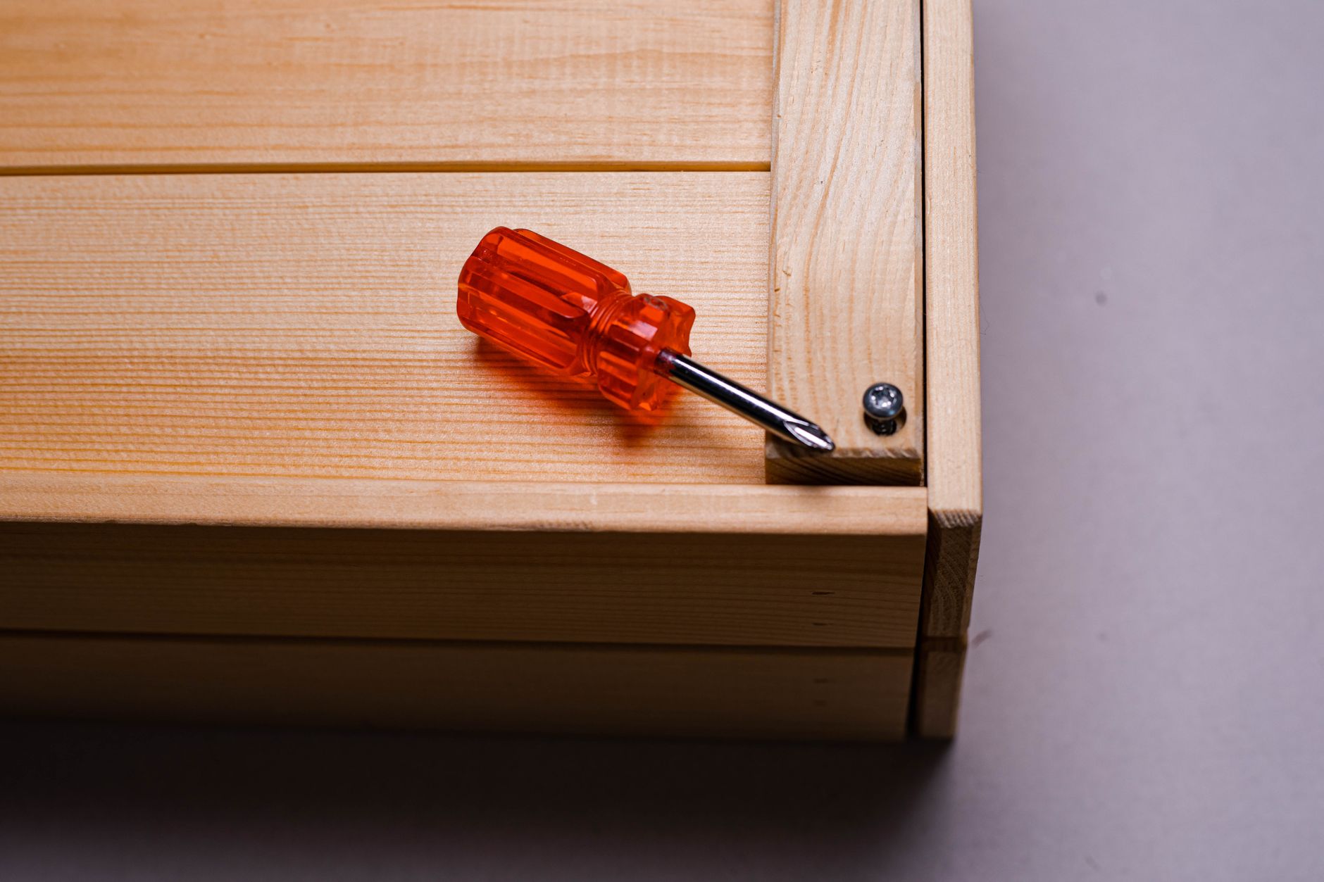 Close-up of an orange screwdriver on a wooden box corner showing precise assembly.