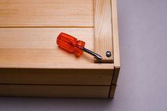 Orange screwdriver on a wooden box corner with screw detail.