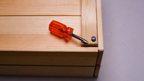 Orange screwdriver on a wooden box corner with screw detail.