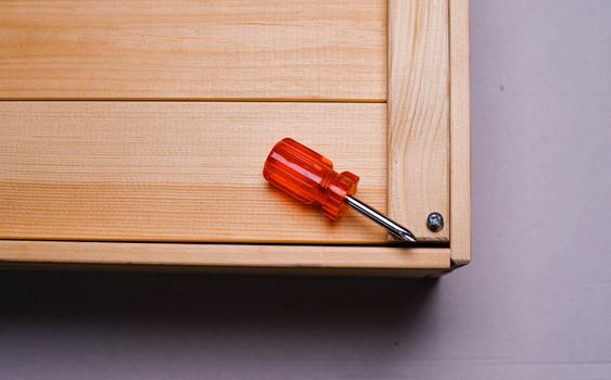 Red-handled screwdriver resting on a wooden box corner, with screws visible.