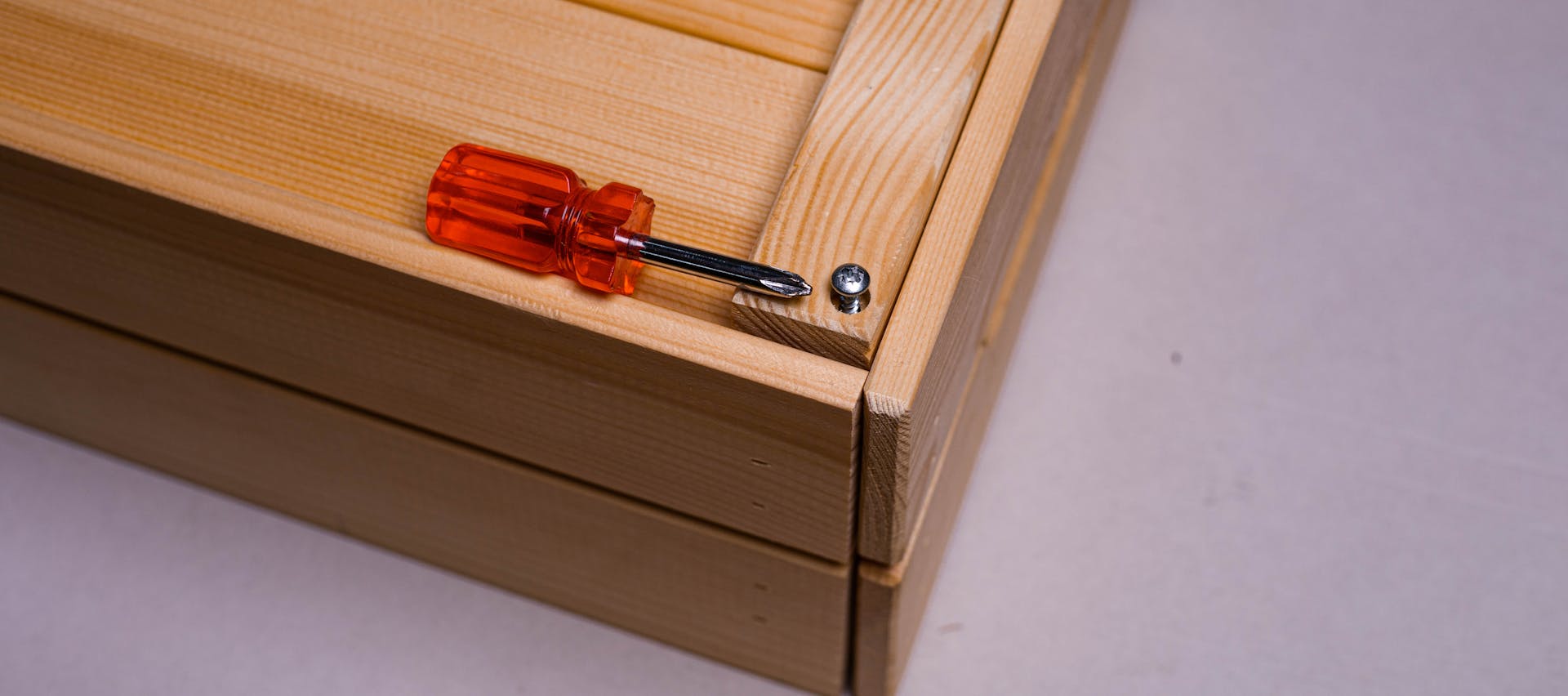 Close-up of orange screwdriver and screw on wooden box edge, perfect for tool-related themes.