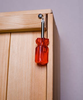 Detailed view of a red-handled screwdriver lodged in a wooden panel.
