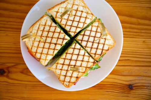 Free Delicious grilled sandwich sliced into quarters on white plate, perfect for lunch. Stock Photo