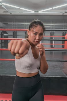 Focused Asian female boxer throwing a punch in an indoor boxing ring environment.