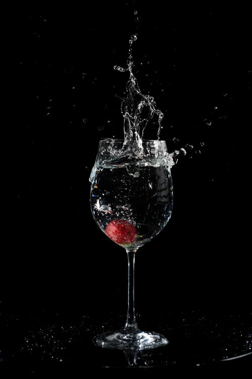 Free A red fruit causing a splash in a wine glass against a black background. Stock Photo