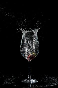Dynamic splash of strawberry in a wine glass captured against a black backdrop, highlighting motion and elegance.