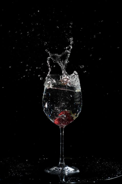 Free A vibrant splash captures motion in a wine glass on black background, highlighting water droplets. Stock Photo