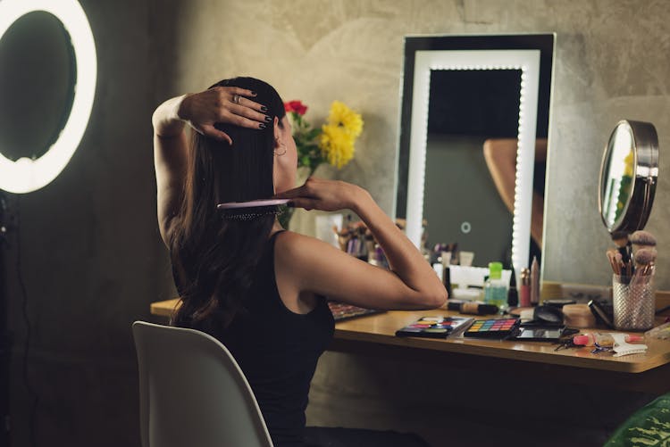 Back View Of A Woman Combing Her Hair In Front Of A Mirror