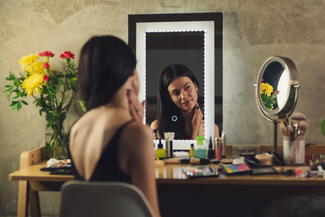 magnifying-mirror-makeup-vanity-detail-work Woman doing makeup at a vanity with a lighted mirror and a small round magnifying mirror