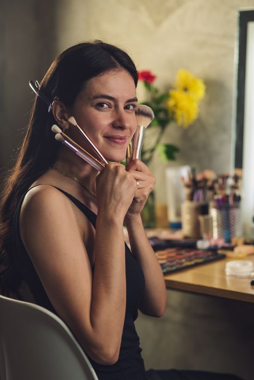 Free A woman happily poses with makeup brushes, showcasing beauty and self-care. Stock Photo
