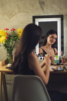 A woman applies makeup at a vanity with yellow and red flowers in a serene setting.