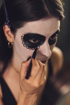 Woman applying intricate Day of the Dead makeup, focusing on eye details, showcasing Mexican tradition and culture.