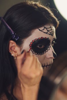A woman is carefully applying traditional Catrina makeup for Day of the Dead celebrations.