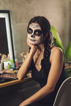 Woman with Catrina makeup seated indoors, reflecting vibrant Mexican cultural style.