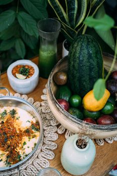Colorful assortment of fruits and refreshing smoothie on a rustic table, surrounded by lush greenery.