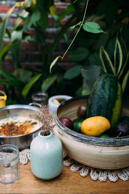 Free A colorful arrangement of fruits and dishes on a rustic wooden table surrounded by lush greenery. Stock Photo