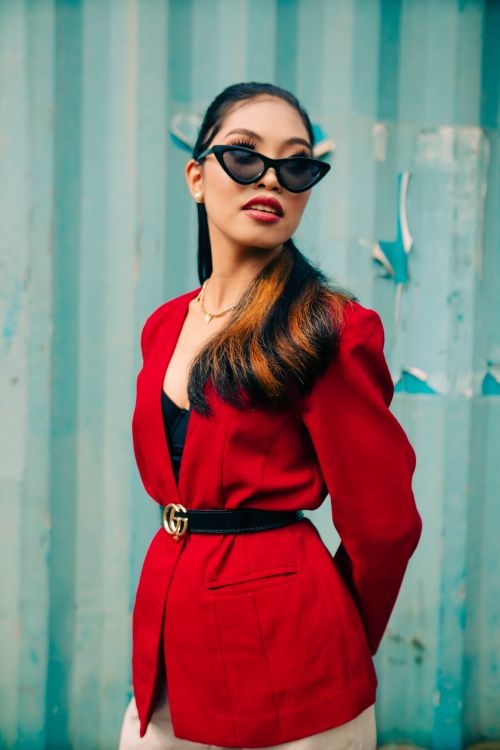 Free Fashionable woman posing in a striking red blazer and sunglasses against a blue background. Stock Photo
