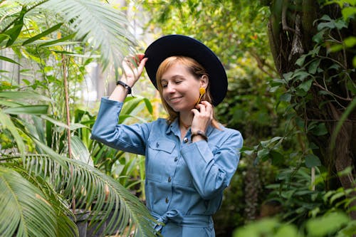 Woman in Blue Dress and Hat Standing Near Green Leaf Plants