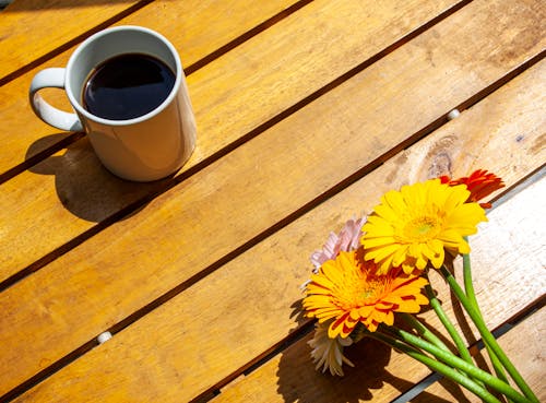 Free Cup of Coffee and Beautiful Flowers on Wooden Surface Stock Photo