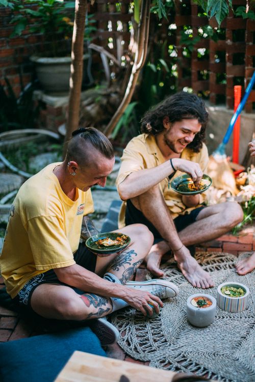 Free Two friends sitting outdoors, enjoying a meal together, with vibrant casual attire and smiling faces. Stock Photo