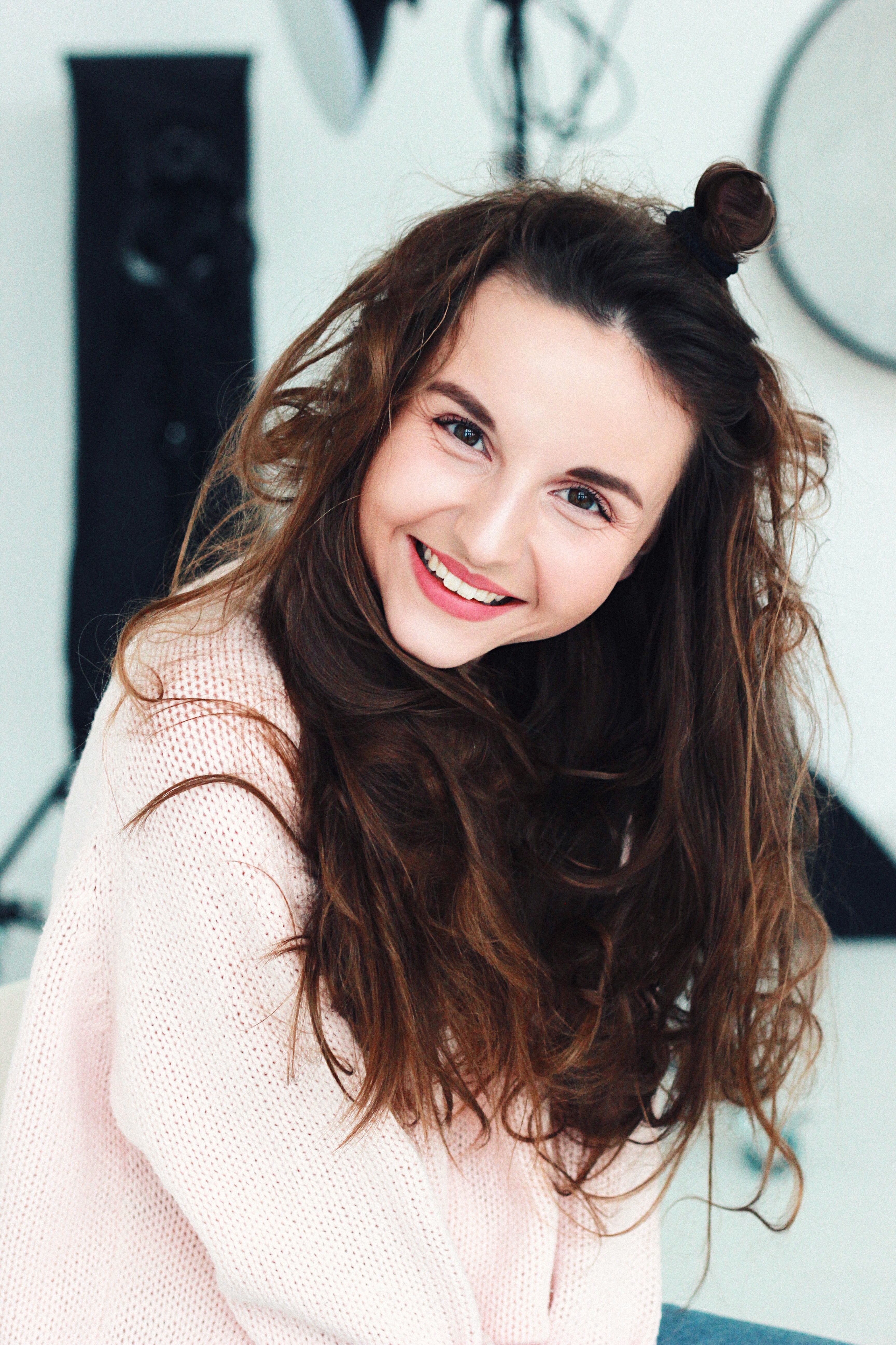 Close-up portrait of a smiling woman with messy hair in a cozy sweater, looking at the camera.