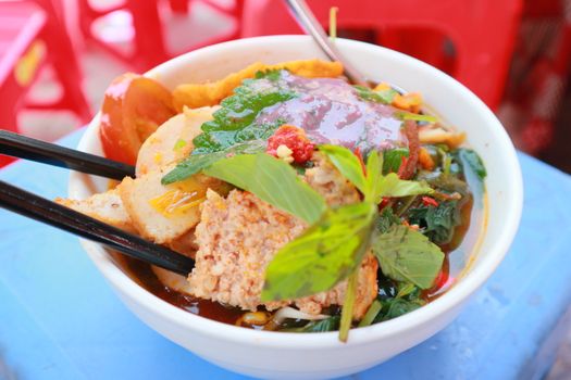 Close-up of flavorful Bun Rieu Cua soup garnished with fresh herbs and vegetables in a bowl.