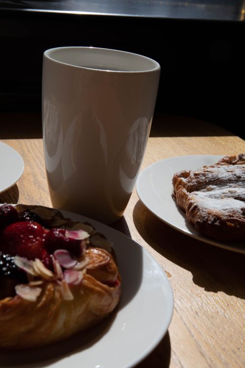 Free Close-up view of assorted pastries and a cup on a wooden table in soft lighting. Stock Photo