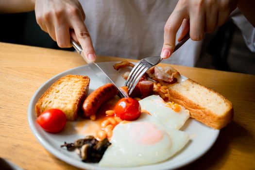 Close-up of a full English breakfast served on a plate with eggs, bacon, sausage, and tomatoes.