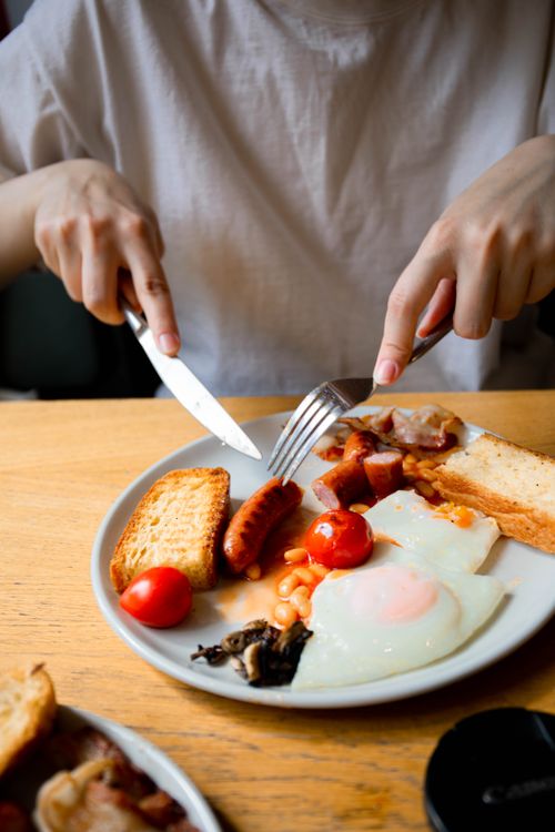 Free A hearty English breakfast with eggs, sausage, tomatoes, and toast on a white plate with wooden table top. Stock Photo