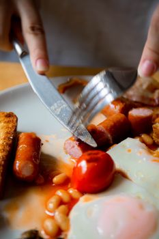 Cutting into sausages on a classic English breakfast plate with beans and fried eggs.