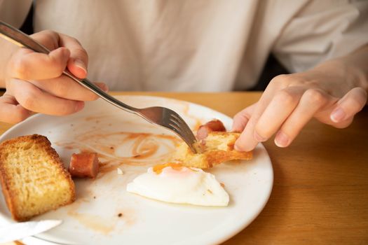 A close-up of a person eating breakfast with toast, egg, and sausage.