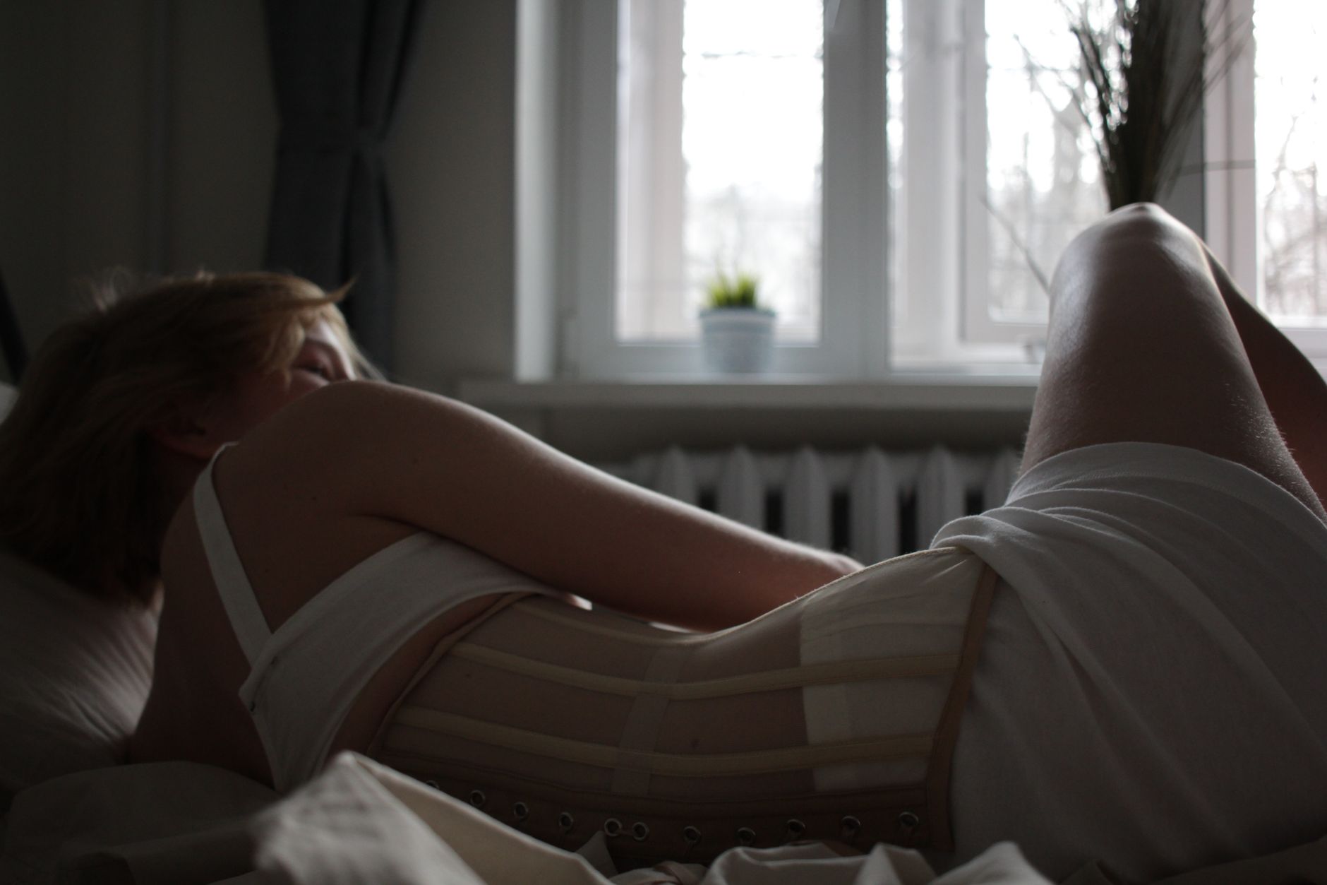 A woman in a corset relaxing on a bed in a dimly lit room.