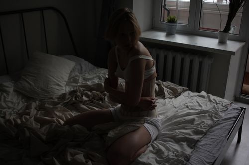 Free A woman in a dimly lit bedroom sits on a bed, creating a moody atmosphere. Stock Photo